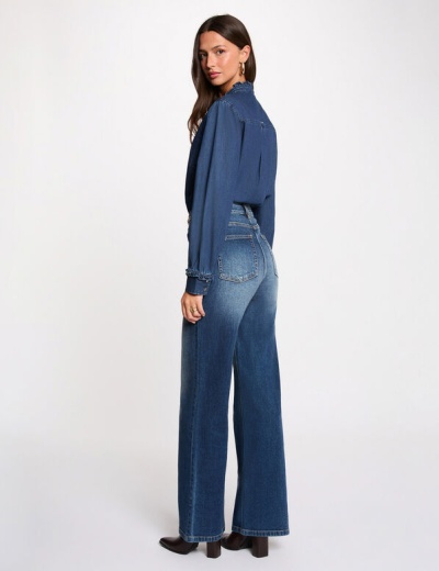 Mulher vestindo calças de ganga azuis e camisa azul escura sobre fundo branco