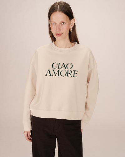 Sweat bege com texto 'CIAO AMORE' usado por mulher sobre fundo neutro