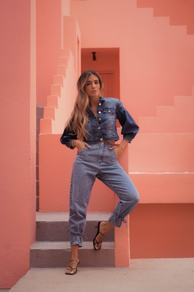 Mulher com casaco e calças de ganga azuis numa escada e parede cor de rosa