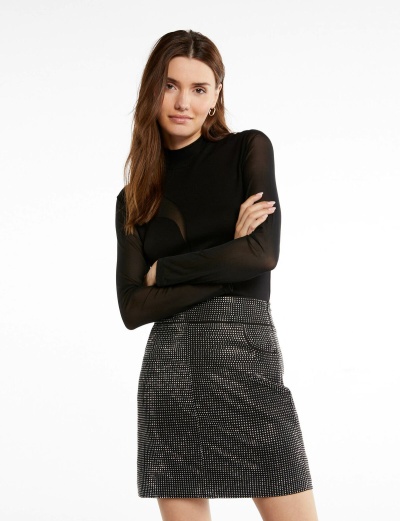 Mulher com top preto de manga comprida transparente e saia curta preta com padrão de pontos brancos.