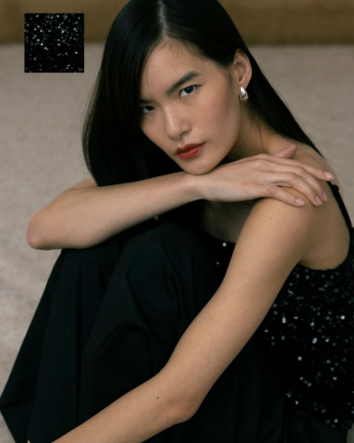 Top preto com lantejoulas usado por mulher com cabelo preto e calças pretas.