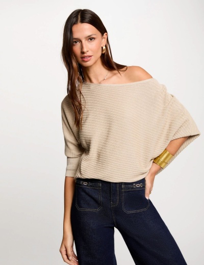 Mulher com camisola bege de malha de riscas e calças jeans escuras num fundo branco