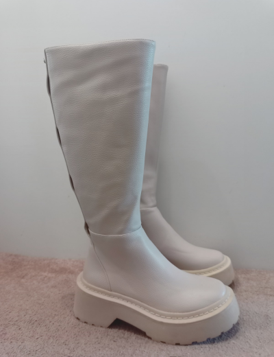 Botas altas creme de couro com sola espessa em superfície rosa.