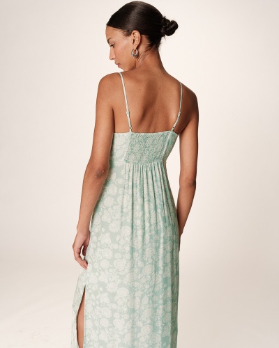 Vestido midi verde claro com padrão floral branco e alças finas, visto de costas, com fenda lateral.
