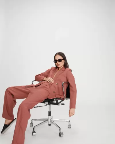 Mulher com fato rosa sentada em cadeira de escritório preta com rodas.