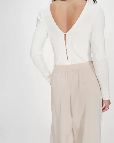 Mulher com camisola branca canelada e calças largas bege vista de costas