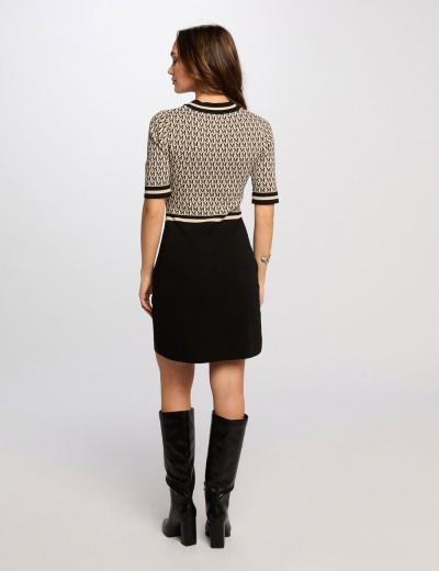 Mulher vista de costas com camisola de padrão geométrico, saia preta curta e botas pretas