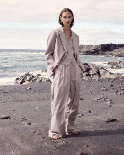 Fato bege claro com riscas finas composto por blazer, colete e calças largas, usado por modelo em praia rochosa.