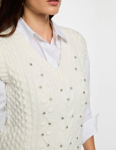 Colete de malha branco com aplicações de contas prateadas por cima de camisa branca