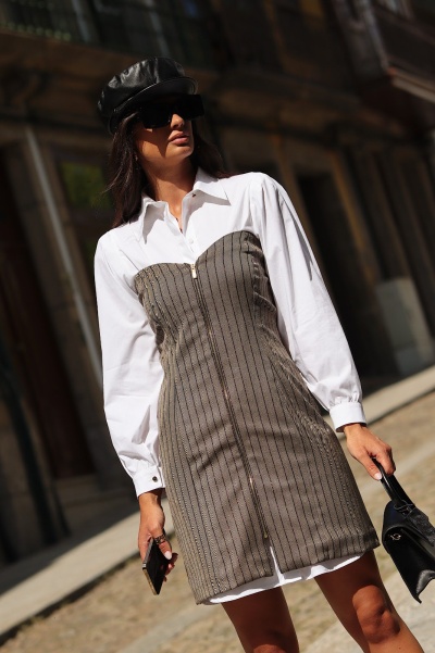 Mulher a usar vestido branco com corpo cinzento riscado e boina preta numa rua urbana