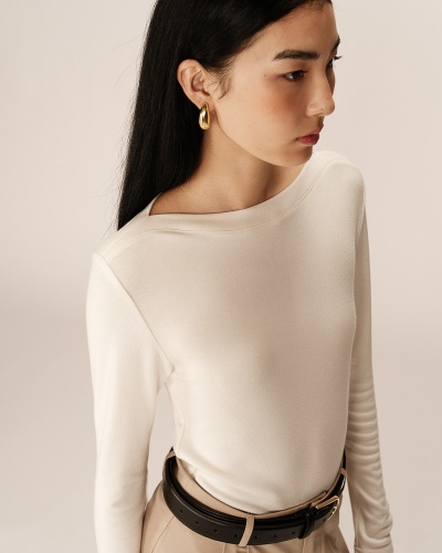 Mulher com camisa branca de manga comprida, calças bege e cinto preto