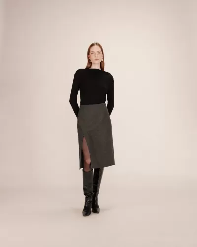 Mulher com blusa preta, saia cinzenta com racha frontal e botas pretas