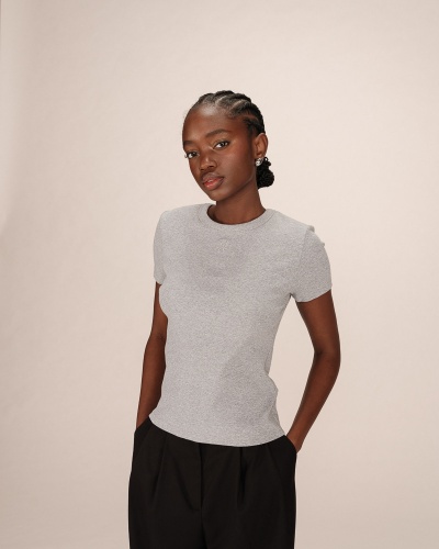 Modelo com t-shirt cinzenta de malha e calças pretas em fundo neutro