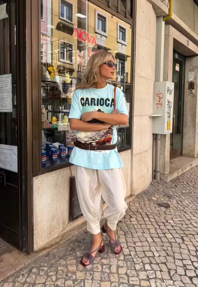 Pessoa com roupa casual e acessórios junto a montra em calçada de pedra
