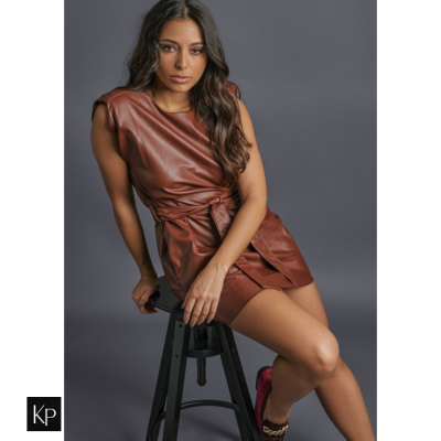 Mulher sentada com vestido castanho curto tipo couro num banco preto