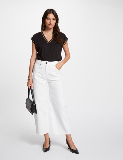 Mulher veste calças brancas largas e top preto, segura mala preta de mão