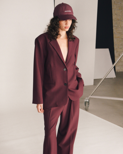 Mulher com blazer e calças bordeaux e boné com texto branco GRACE & MILA