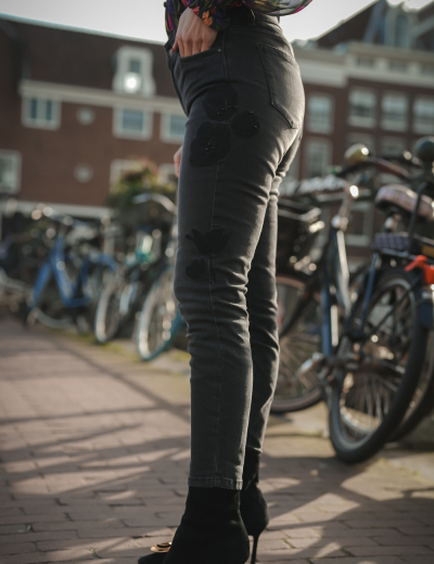 Calças justas pretas com padrão de flores pretas, em ambiente urbano com bicicletas ao fundo