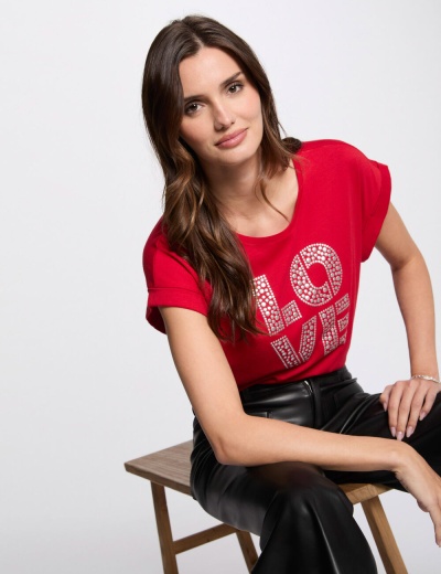 Mulher sentada com camiseta vermelha  LOVE e calças pretas
