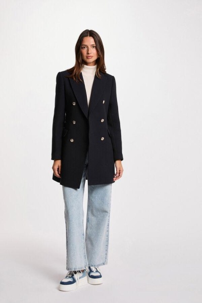 Casaco preto de lã com botões dourados, mulher com jeans claros e sapatilhas azuis e brancas