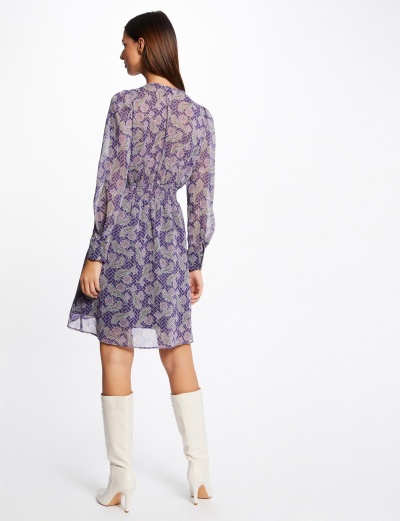 Vestido curto transparente com padrão roxo e azul, mangas compridas, usado com botas brancas, vista traseira.