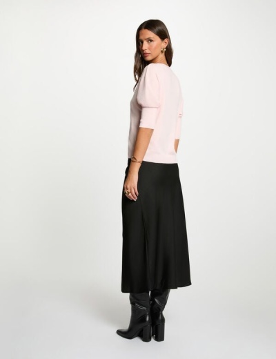 Mulher de costas com camisola rosa, saia preta longa e botas pretas