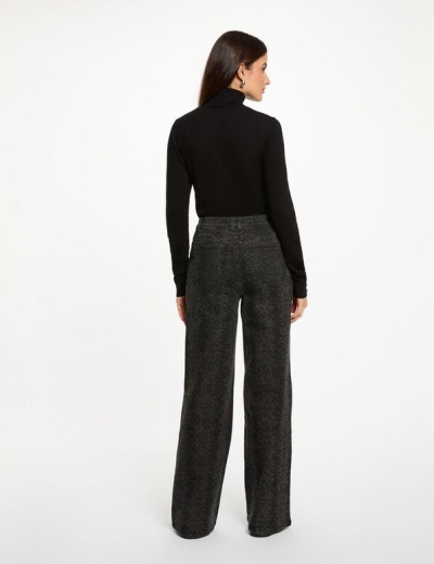 Mulher de costas a usar calças largas cinza escuro com padrão e camisola preta de gola alta.