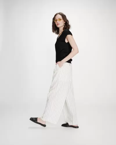 Mulher a usar calças brancas às riscas e top preto, com óculos de sol amarelos