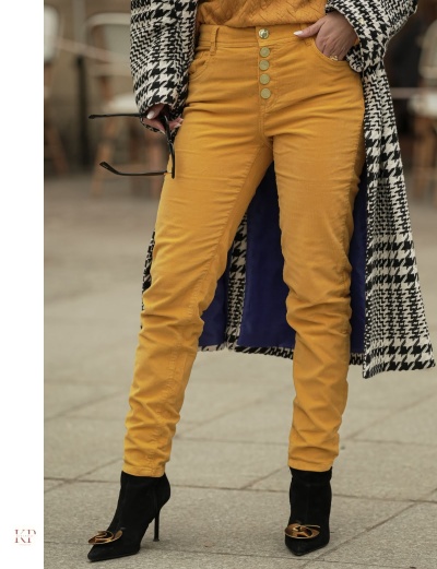 Calças amarelas com botões dourados, botas pretas de salto e casaco pied-de-poule preto e branco.