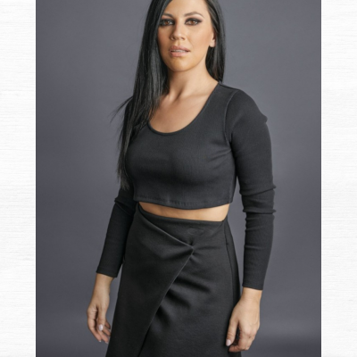 Mulher vestindo blusa preta de manga comprida e saia preta com design cruzado.