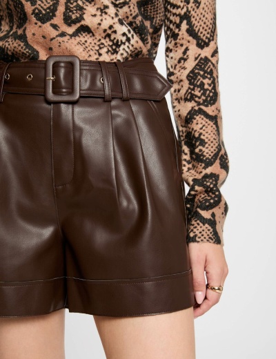 Calções castanhos escuros em tecido semelhante a couro com cinto largo e camisa de malha com padrão animal print.