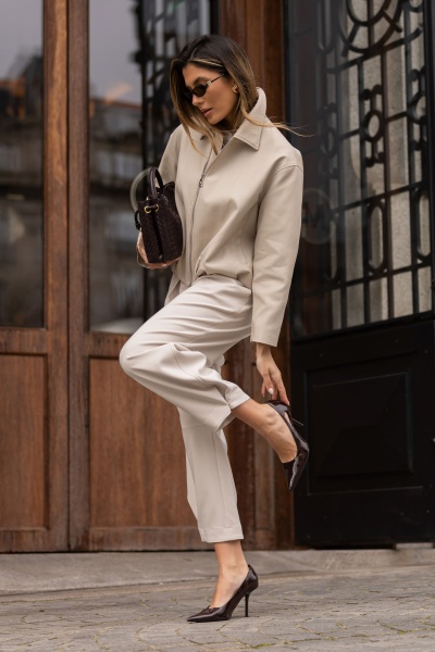 Mulher de casaco bege, calças bege e sapatos de salto pretos com mala castanha escura