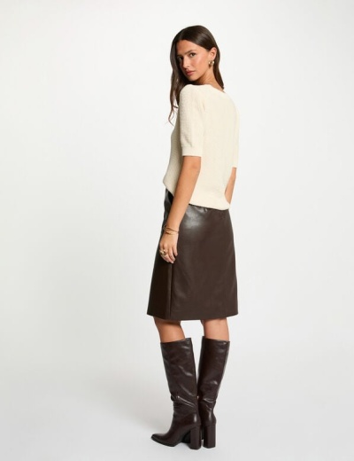 Mulher com camisola creme, saia castanha escura de couro e botas castanhas altas.