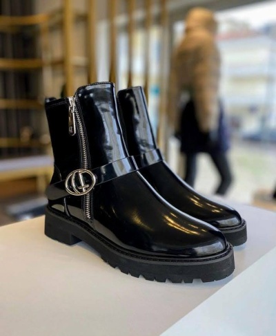 Botas pretas brilhantes com fivela metálica e fecho lateral sobre mesa branca