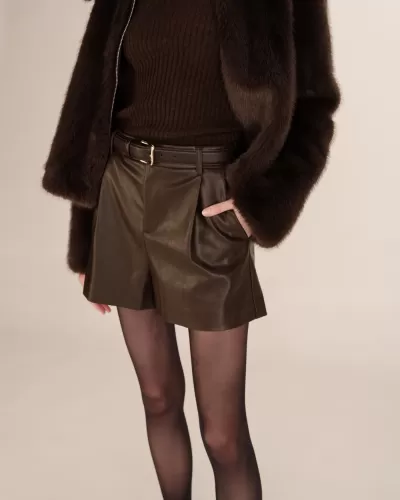 Calções de pele castanho escuro com cinto, camisola de malha castanha, casaco de pelo castanho e meias pretas transparentes