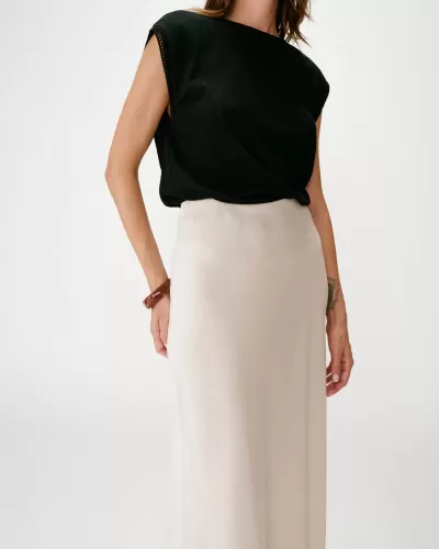 Mulher com blusa preta sem mangas e saia comprida bege em fundo branco