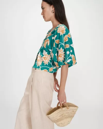 Mulher com blusa floral verde, calças bege e bolsa de palha
