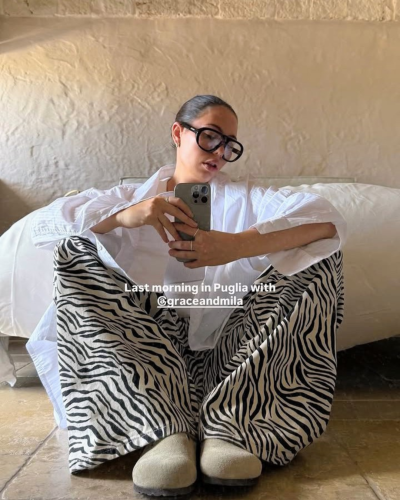 Mulher com calças zebras preto e branco, camisa branca e óculos grandes sentado no chão