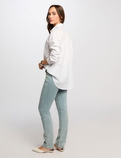 Mulher com calças de ganga azuis claras, camisola branca e sapatos brancos num fundo branco.