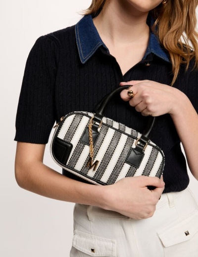 Mala pequena às riscas pretas e brancas com detalhes dourados, segurada por mulher com camisa preta e calças brancas