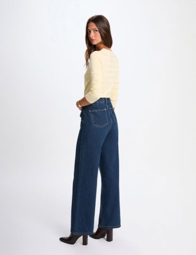 Mulher de costas com calças de ganga azuis e camisola creme em fundo branco