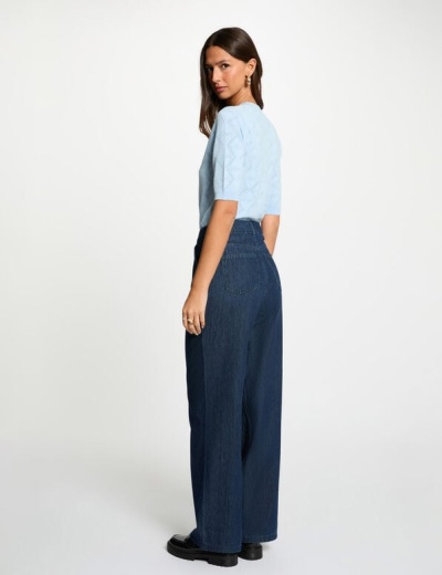 Mulher a usar camiseta azul clara e calças largas de ganga azul escuro em fundo branco