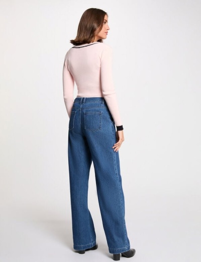 Mulher vista de costas com calças de ganga largas azuis, camisola rosa e botas pretas