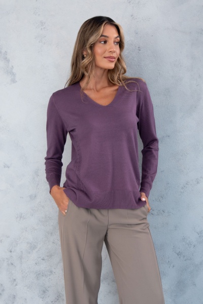 Camisola roxa de malha com decote em V e calças bege numa mulher, fundo cinzento texturizado