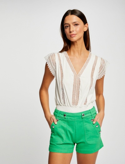 Mulher com blusa branca de renda e calções verdes com botões