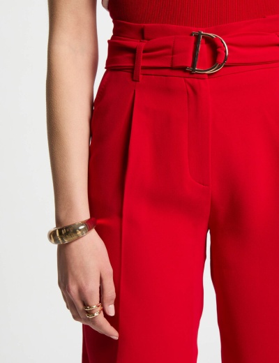 Top vermelho de malha com calças vermelhas e cinto largo com fivela D dourada, pulseira e anéis dourados