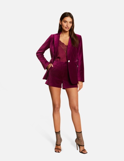 Mulher a usar conjunto de blazer e calções em veludo vinho com top rendado e sandálias de salto alto