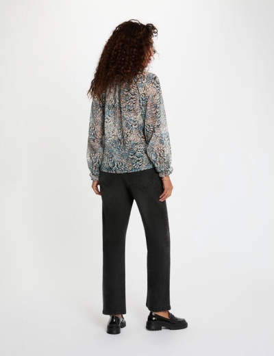 Mulher de costas com camisa estampada e calças pretas num fundo branco