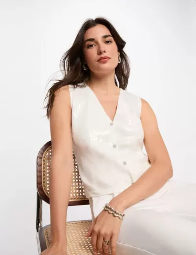 Colete branco feminino sentado numa cadeira de metal com assento em vime