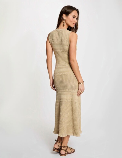 Mulher de costas vestindo vestido comprido bege com texturas detalhadas e sandálias com tachas